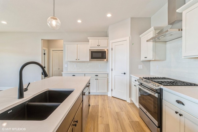 kitchen featuring a sink, white cabinets, appliances with stainless steel finishes, wall chimney exhaust hood, and light wood finished floors