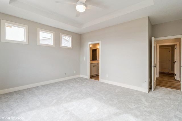 unfurnished bedroom with baseboards, a raised ceiling, ensuite bath, ceiling fan, and carpet