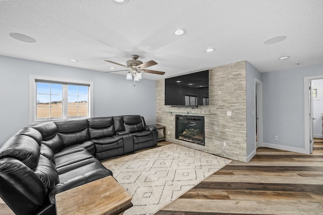 living room featuring light hardwood / wood-style floors, a textured ceiling, a stone fireplace, and ceiling fan