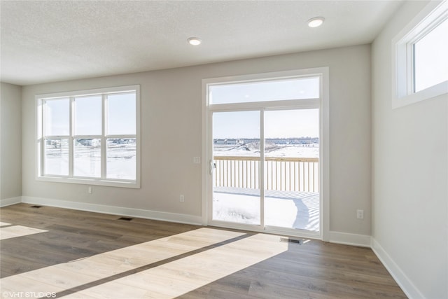 spare room with dark wood-style flooring, visible vents, and baseboards