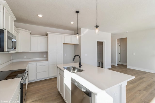 kitchen featuring hanging light fixtures, a kitchen island with sink, stainless steel appliances, light countertops, and a sink