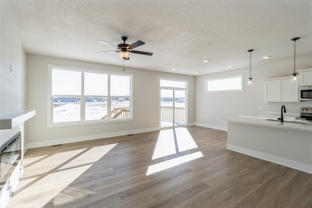 living area with recessed lighting, a glass covered fireplace, a textured ceiling, wood finished floors, and baseboards