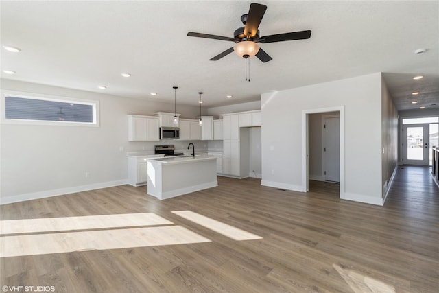 kitchen featuring stainless steel appliances, light countertops, open floor plan, white cabinets, and a kitchen island with sink