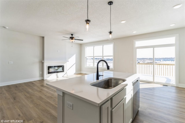 kitchen featuring a sink, light countertops, gray cabinets, an island with sink, and decorative light fixtures