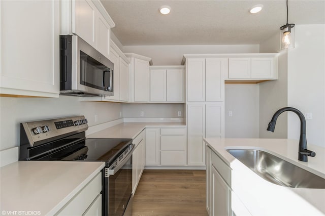 kitchen with appliances with stainless steel finishes, hanging light fixtures, light countertops, white cabinetry, and a sink