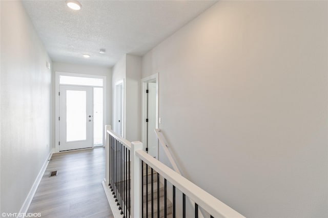 corridor featuring light wood-type flooring, visible vents, a textured ceiling, and baseboards