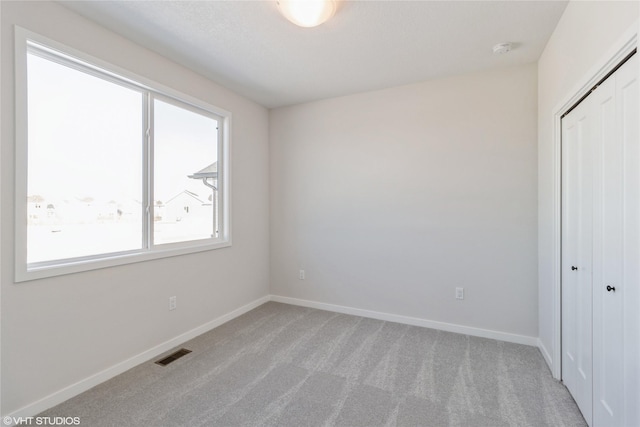 unfurnished bedroom with light colored carpet, a closet, visible vents, and baseboards