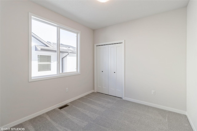 unfurnished bedroom with a closet, visible vents, light carpet, and baseboards