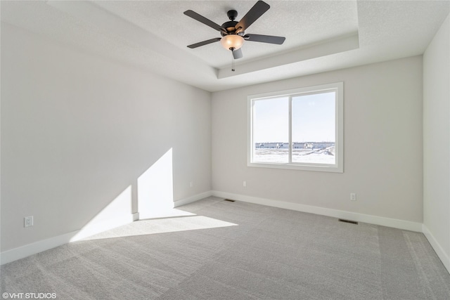 spare room featuring a tray ceiling, light carpet, a textured ceiling, and baseboards