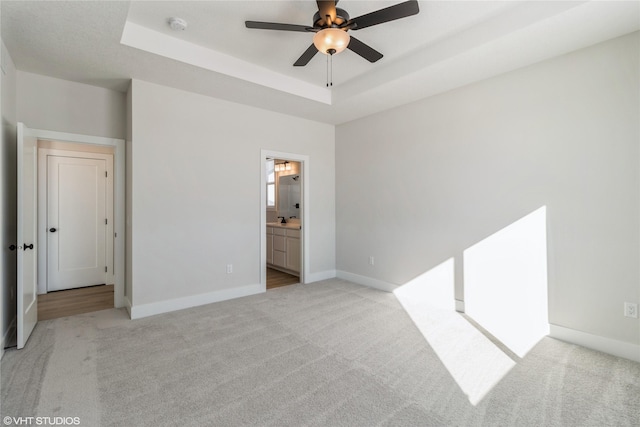 unfurnished bedroom with a raised ceiling, light carpet, and baseboards