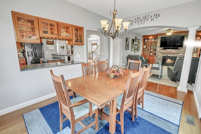 dining area featuring decorative columns, a stone fireplace, dark hardwood / wood-style floors, and ceiling fan with notable chandelier