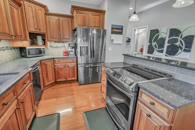 kitchen with backsplash, appliances with stainless steel finishes, dark stone countertops, pendant lighting, and light hardwood / wood-style floors