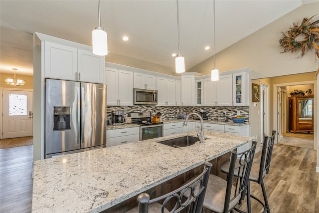 kitchen featuring stainless steel appliances, sink, vaulted ceiling, pendant lighting, and white cabinets