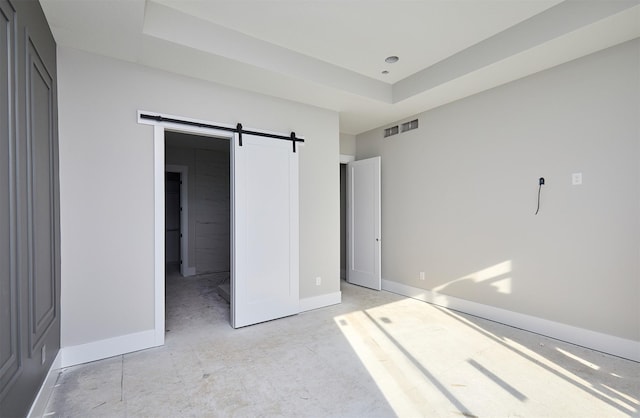 unfurnished bedroom featuring a barn door and a raised ceiling