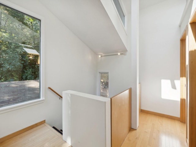 hall with baseboards, an upstairs landing, and hardwood / wood-style flooring