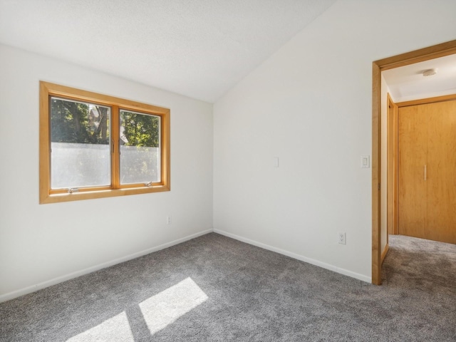 spare room featuring carpet flooring, vaulted ceiling, and baseboards