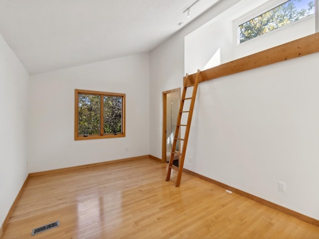 spare room with baseboards, visible vents, vaulted ceiling, and wood finished floors