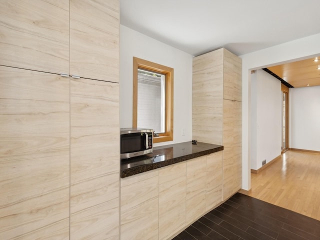 kitchen with baseboards, light brown cabinetry, stainless steel microwave, modern cabinets, and dark wood finished floors