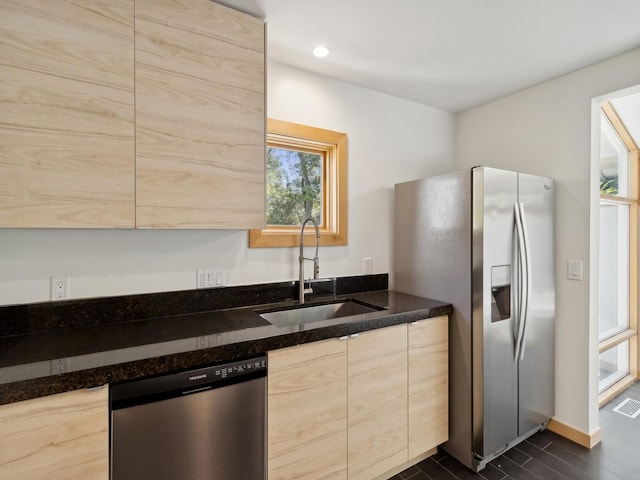 kitchen featuring recessed lighting, light brown cabinetry, appliances with stainless steel finishes, a sink, and dark stone counters