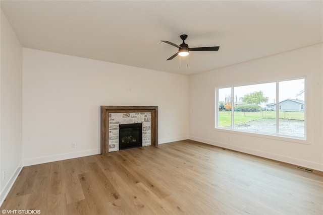 unfurnished living room with light wood-type flooring, a stone fireplace, and ceiling fan