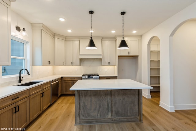 kitchen with light hardwood / wood-style flooring, sink, a kitchen island, hanging light fixtures, and appliances with stainless steel finishes