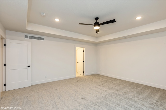 unfurnished room with a raised ceiling, ceiling fan, and carpet