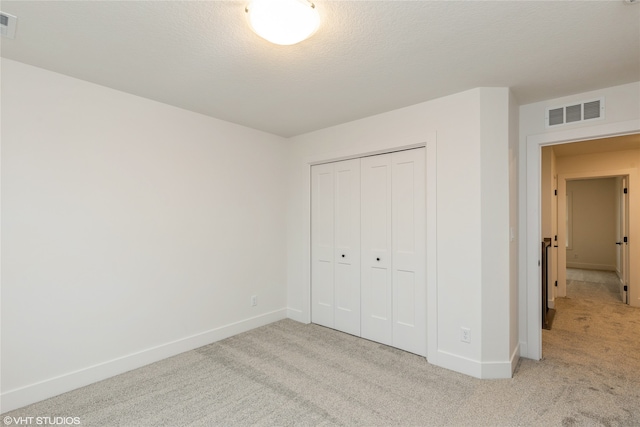 unfurnished bedroom with a closet, light colored carpet, and a textured ceiling