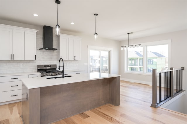 kitchen with a center island with sink, wall chimney exhaust hood, light hardwood / wood-style floors, and white cabinets