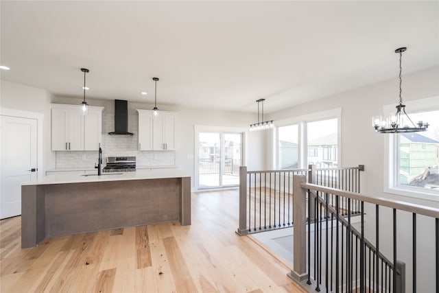 kitchen featuring sink, wall chimney range hood, a center island with sink, white cabinets, and light hardwood / wood-style floors