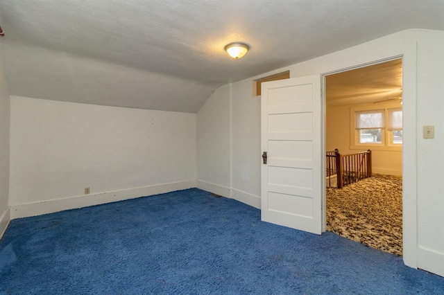 additional living space featuring a textured ceiling, dark carpet, and vaulted ceiling