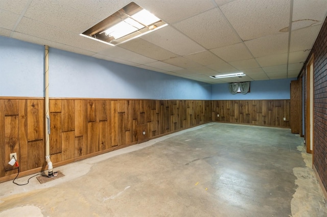 basement featuring brick wall, a drop ceiling, and wood walls