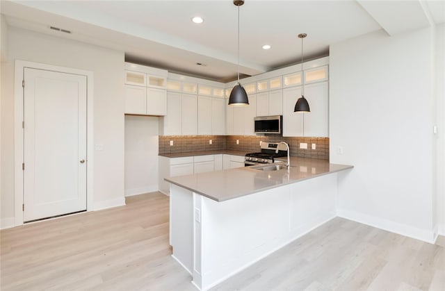 kitchen with kitchen peninsula, stainless steel appliances, decorative light fixtures, white cabinets, and light hardwood / wood-style flooring