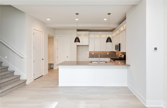 kitchen featuring hanging light fixtures, kitchen peninsula, sink, white cabinets, and appliances with stainless steel finishes