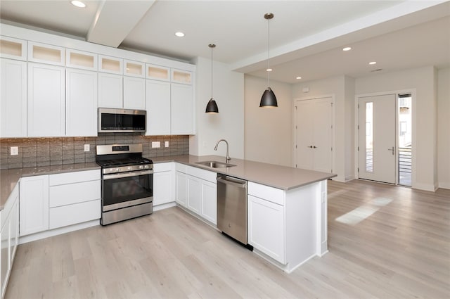 kitchen with appliances with stainless steel finishes, sink, hanging light fixtures, white cabinetry, and light hardwood / wood-style flooring