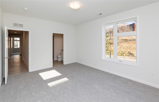 unfurnished bedroom featuring multiple windows, light colored carpet, and connected bathroom