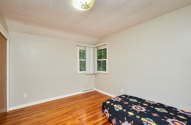 unfurnished bedroom featuring lofted ceiling, a textured ceiling, hardwood / wood-style flooring, and a baseboard heating unit