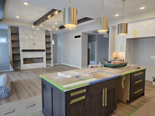 kitchen featuring light wood-type flooring, beam ceiling, decorative light fixtures, a kitchen island, and dark brown cabinets