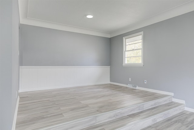 unfurnished room with baseboards, visible vents, wainscoting, and light wood-style floors
