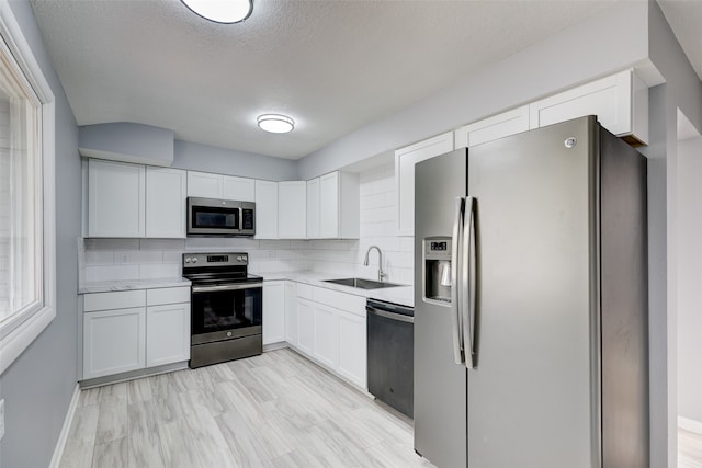 kitchen with appliances with stainless steel finishes, white cabinets, sink, and backsplash