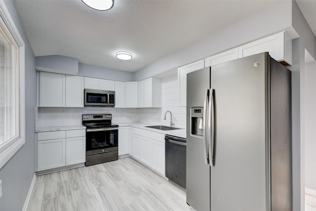 kitchen with decorative backsplash, stainless steel appliances, light countertops, a sink, and white cabinetry