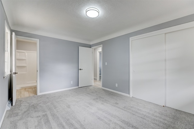 unfurnished bedroom with a textured ceiling, light carpet, ensuite bathroom, and a closet