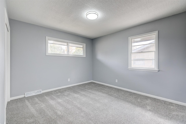 carpeted spare room with a textured ceiling, visible vents, and baseboards