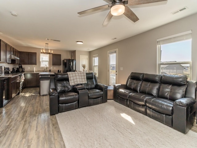 living room featuring visible vents, wood finished floors, and ceiling fan with notable chandelier