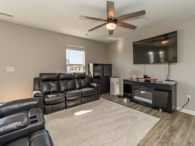 living room featuring ceiling fan, wood finished floors, visible vents, and baseboards