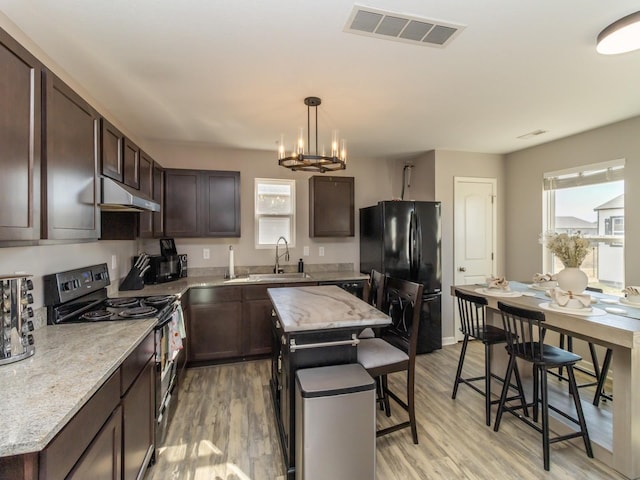 kitchen featuring visible vents, freestanding refrigerator, dark brown cabinetry, range with electric cooktop, and under cabinet range hood