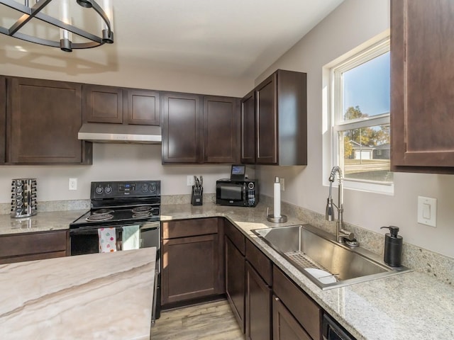 kitchen featuring dark brown cabinetry, under cabinet range hood, a sink, light wood-type flooring, and black appliances