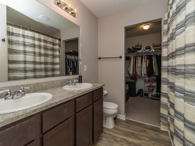 full bath with double vanity, a sink, toilet, and wood finished floors