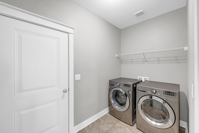 clothes washing area with independent washer and dryer, a textured ceiling, and light tile patterned floors