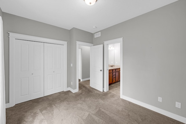 unfurnished bedroom with ensuite bathroom, a closet, and light colored carpet