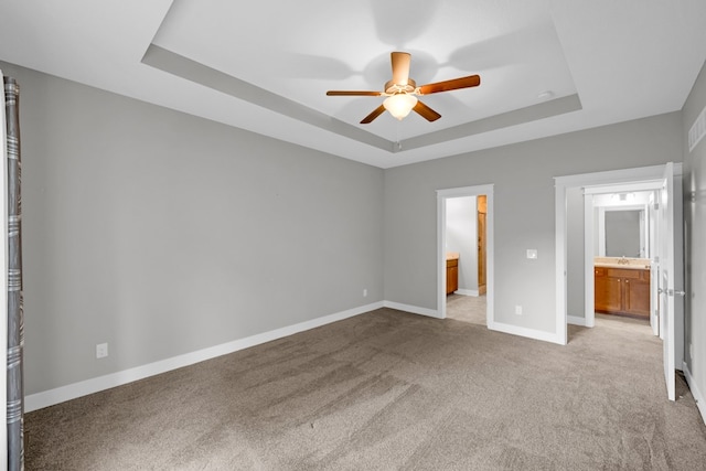 unfurnished bedroom featuring connected bathroom, ceiling fan, light carpet, and a tray ceiling